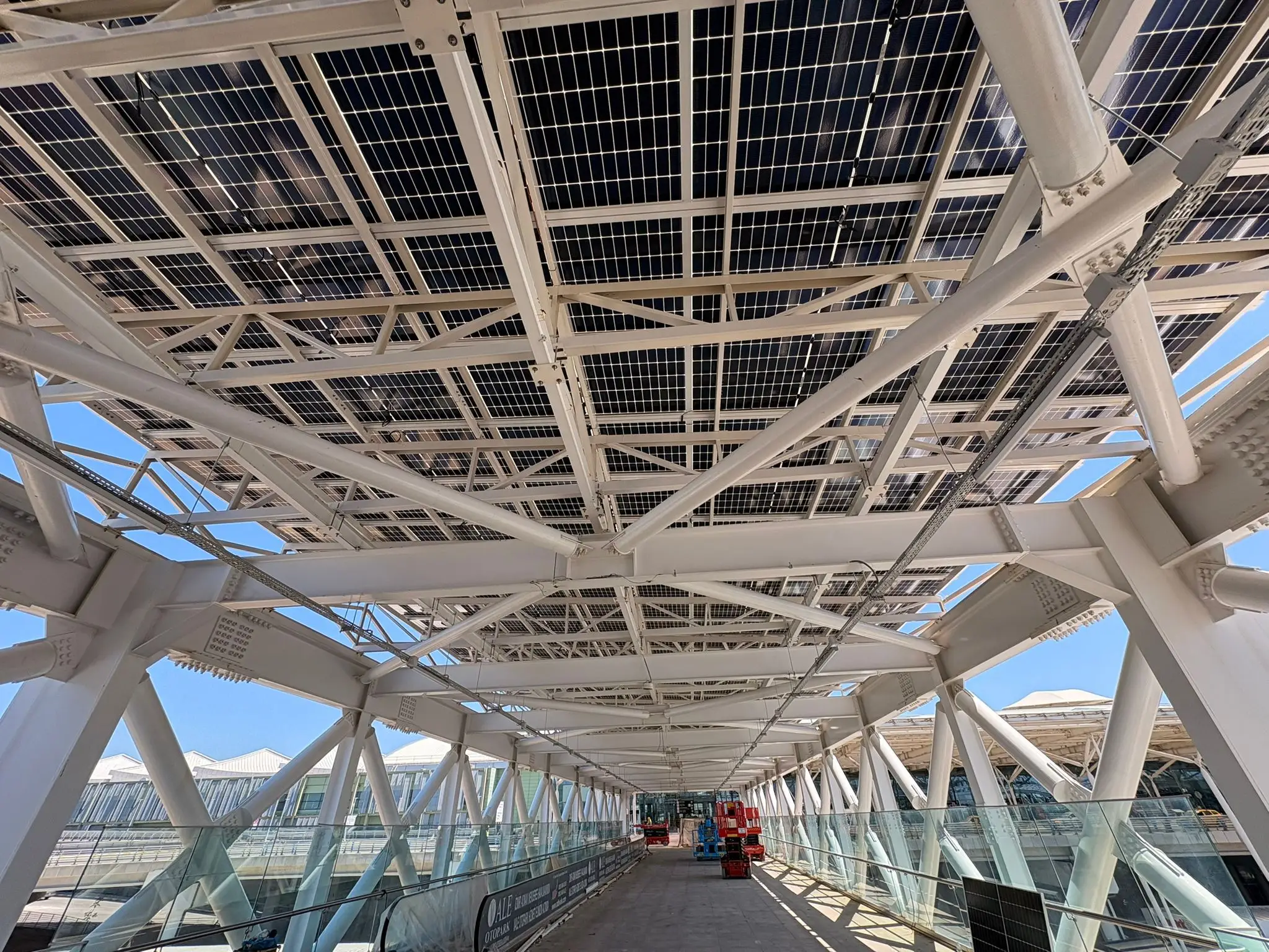Tamamlanmış güneş enerjili carport kanopisinin altından yukarı bakış; çelik taşıyıcılar ve güneş panelleri